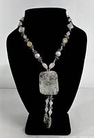 Front view of the necklace on display showing the large rectangular rutilated quartz pendant and the beaded chain with varied stones and colors.