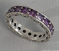 Side angle showing silver ring band with purple stones set along outside and engraved infinity leaf pattern on edges.
