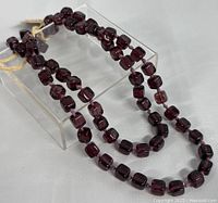 Full view of the garnet bead necklace laid over a clear stand highlighting bead shape and color.