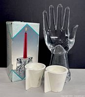 Clear glass hand sculpture standing beside two clear glass ice cube candle holders and original box with candle holder image.