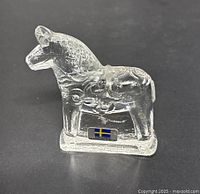Clear crystal glass horse figurine with Swedish flag sticker on the base front view on black background.