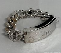 Silver tone Dior lip gloss bracelet with rectangular centerpiece plate engraved "Dior." Minor surface wear and tarnish visible.