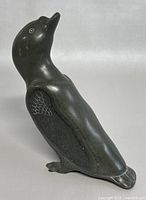 Side view of the polished dark stone bird sculpture showing engraved wing and tail feather details, slight surface wear visible.