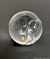 Crystal tennis ball paperweight showing smooth polished surface with etched groove details, reflecting light with some minor wear.