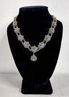 Front view of the full necklace on display stand showing floral turquoise and coral medallions linked by brass.