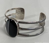 Angled view of the vintage sterling silver cuff bracelet showing black onyx oval stone with white stripes and triple band design.