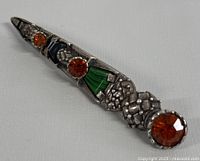 Close-up of vintage Miracle Scottish Celtic sword brooch showing detailed metalwork and orange, green, blue, purple gemstones.