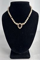Front view on black stand showing the pearl necklace with black and rhinestone teardrop clasp