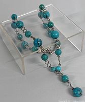 Full view of turquoise bead necklace displayed on a clear stand showing bead size variation and chain linking.