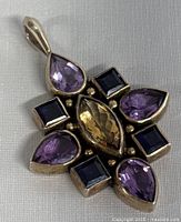 Front view of the vintage sterling silver pendant showing amethyst, dark blue square gemstones, and central yellow marquise-shaped gemstone.
