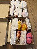 Top view of two open cardboard boxes showing some of the glass figurine ornaments individually wrapped in white tissue paper.
