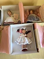 Three boxed Madame Alexander 4th of July dolls, showing their dresses and boxes with pink tissue paper, some staining visible on boxes.