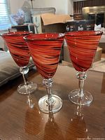 Photo showing three tall stem glasses with swirl color patterns in red shades on a table.