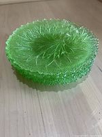 Stack of green glass plates with embossed leaf pattern, showing textured glass and scalloped edges