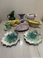 Full group of 8 ceramic pottery pieces arranged on a table showing various shapes, colors, and glaze finishes.