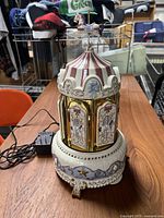 Ceramic musical carousel on table with power adapter. Front view showing carousel with door and horse figure on top.