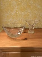 Pair of Steuben Glass Thumbprint trumpet vase and lead crystal bowl on a wooden surface against a beige textured wall.