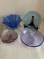Set of 4 vintage art glass items: two bowls in blue and purple, a light blue plate, and a small purple bowl.