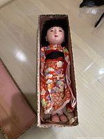 Full view of vintage Japanese doll dressed in traditional red floral kimono inside original box.