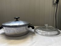Photo showing hammered aluminum casserole dish with vented lid, black and silver Bakelite handles and knob, and FireKing glass lid separate
