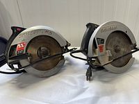 Two Skilsaw circular saws side by side showing metal blade guards, handles and power cords.