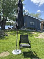 Charcoal grey 9 ft Sunbrella patio umbrella in closed position next to black folding chair on grass near lake house.