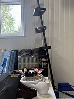 Photo shows black metal shower caddy with four shelves, four baseball hats, Stanley travel mug, and Mr. and Mrs. Wonderful talking dolls sitting on a white container near a wall.