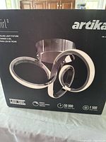 Front side of the box showing the Artika LED swirl light fixture in chrome finish, indicating 50,000 hours lifespan and 1500 lumens brightness.