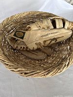 Baseball mitt resting inside round woven basket, showing mitt details and mitt size.