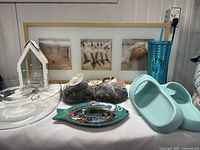 Full lot display on table including framed beach art, glass bowl, decorative fish dish, river rocks, sandals, Starbucks cup, and lantern.