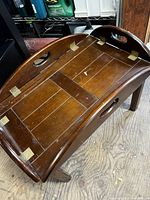 Angled view of the wooden serving tray showing brass hinges, surface scratches, and integrated handles.