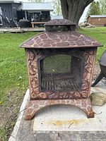 Front view of cast iron outdoor fireplace with textured stone-like surface and black mesh door.
