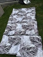 Photo showing all four outdoor chair cushions laid flat on grass. Cushions have tufted padding and a gray, white, and muted purple leaf print.