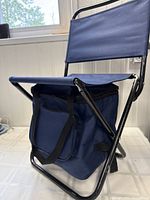 Side view of the blue foldable chair showing seat, backrest, metal frame and cooler compartment beneath seat with handles.