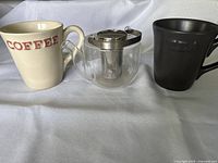 Photo showing the set with glass infuser pot in the center, cream 'COFFEE' mug on left, black 'TEA' mug on right on white background