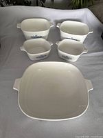 Front view of five white ceramic Corningware casserole dishes with blue cornflower pattern, 2 large, 2 small, 1 shallow dish.