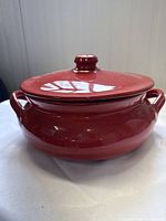 Side view of a glossy red terracotta crock pot with two handles and a fitted lid with a knob.
