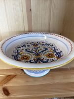Side view of hand-painted ceramic fruit bowl on pedestal, showing scalloped rim and floral pattern.
