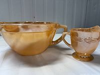 Photo shows FireKing Peach Lustre pitcher and creamer side by side, highlighting their peach lustre color and iridescent finish.