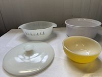 View of three casseroles: yellow FireKing bowl, white FireKing casserole with blue starburst pattern, white Corningware casserole, and white lid