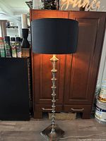 Full view of the 5 ft tall floor lamp with metallic segmented stand and black drum shade.
