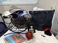 Photo of the black vegan snakeskin tote bag with hanging makeup bag, several hats on iron twisted wine rack, white summer top, cologne bottle, journals, and hair accessories.