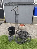 Full lot showing garden hose, four pots, tri-pot, and garden trellis against shed and gravel ground.