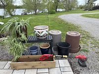 Full lot image showing spider plants in vintage bucket, ceramic pots, plastic planters, cedar box, electric whipper/snipper, and garbage cans outside on paved surface by road.