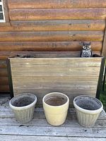 Large cedar planter box with soil and ceramic garden pots in front, owl decoration visible inside box