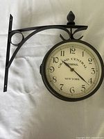 Side view of double-sided Grand Central style wall clock showing the black metal mounting bracket and one clock face.