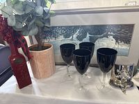 Photo showing red Pier 1 vinegar bottle, faux eucalyptus plant in beige pot, four black wine glasses with black bowls and clear stems, framed Michael Dumas bunny print, and a silver snowflake mantle hook.