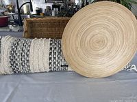 Two DKNY large bolster accent pillows, woven basket, and large wood centerpiece plate on table