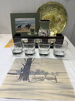 Photo of framed and unframed art prints by James Bessey alongside the Jack Daniels rock glasses and gold charger plate vase and candle holder, with wooden tealight shelf at the back.