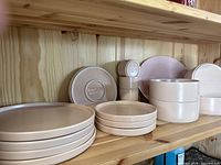Wooden shelf with stacked dinner plates, salad plates, bowls and pastel platter visible